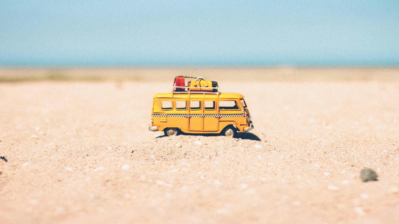 A toy van on a sandy beach evokes summer travel and vacation vibes.