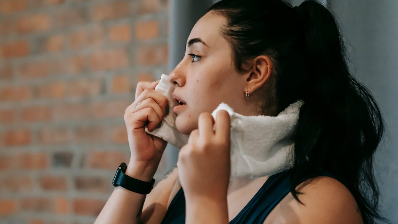 Side view of a woman wiping sweat with a towel after exercising indoors.