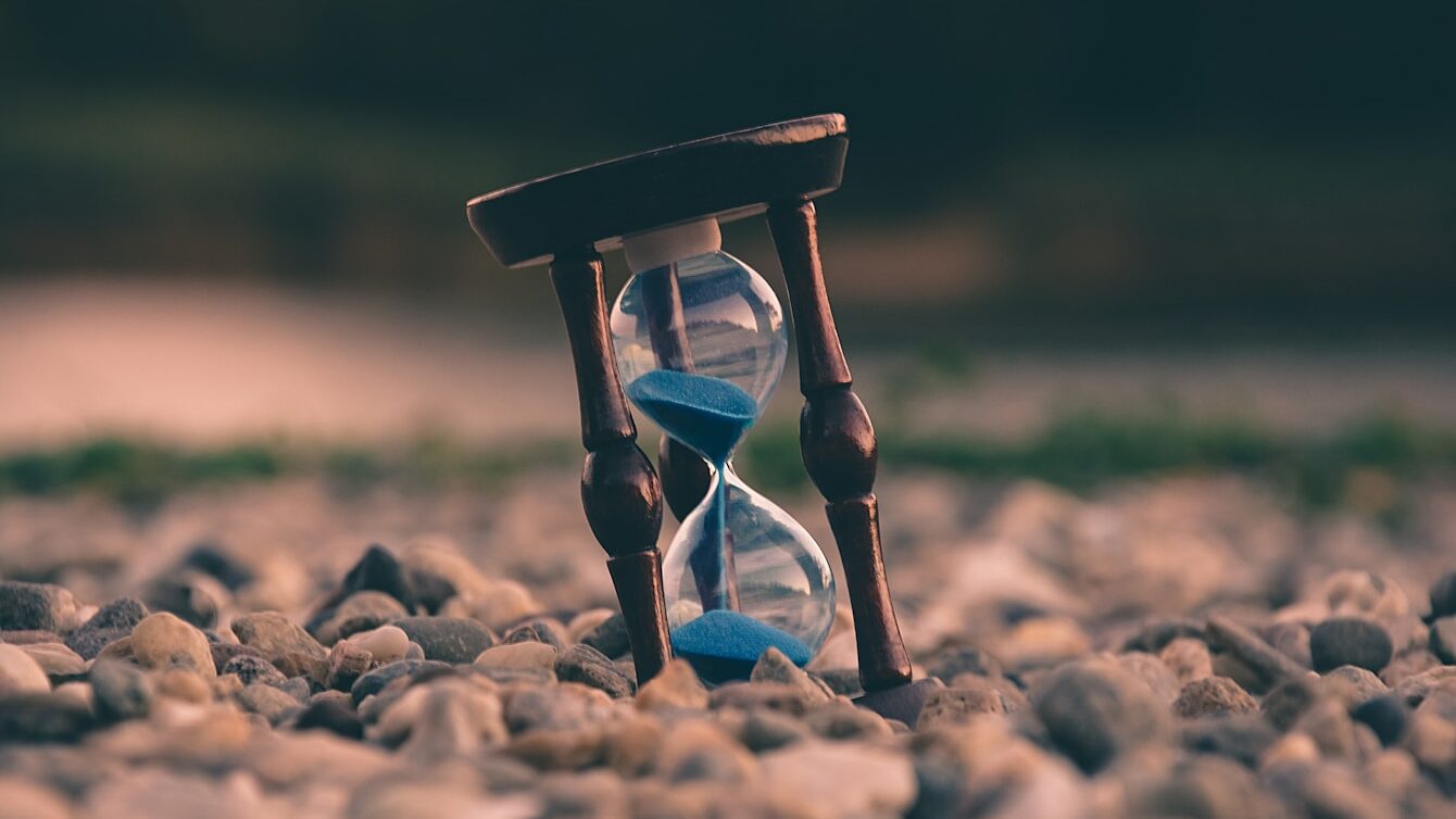 selective focus photo of brown and blue hourglass on stones